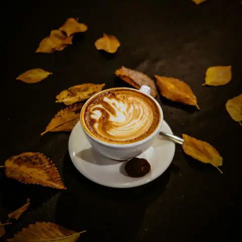 Sonbahar yaprakları arasında latte art'lı kahve